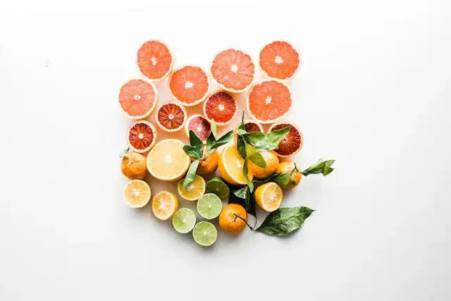 Flat lay of halved citrus fruits including grapefruit, lime, bergamot, and lemon arranged on a white background with fresh green leaves—symbolizing zesty, natural ingredients used in clean, uplifting aromatherapy.