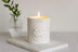 White candle labeled 'Cupid' on a marble coaster with a vase of greenery in the background