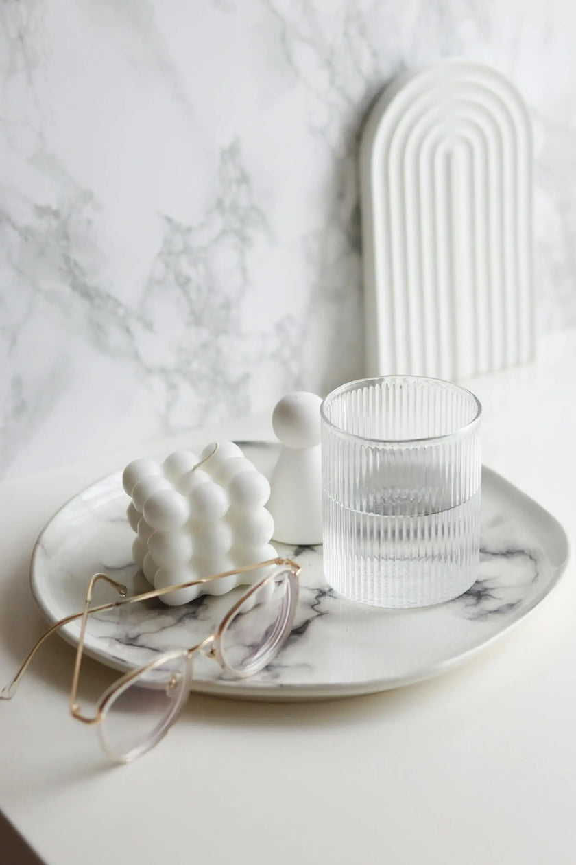 White ceramic dish with a glass, small sculpture, and eyeglasses on a marble surface