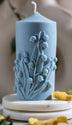 Handcrafted blue pillar candle with intricate lily of the valley floral design, perfect for elegant home décor.