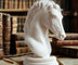 White horse bust on a wooden surface with books in the background