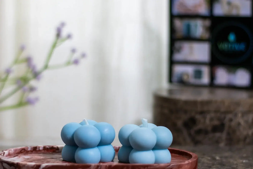 Three blue candles stacked on a pink ceramic plate with a blurred background