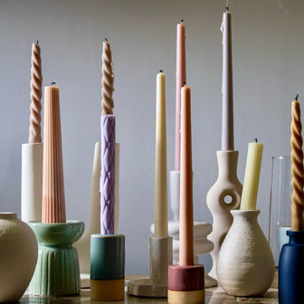 Collection of colorful candles and ceramic holders on a wooden surface with a neutral background