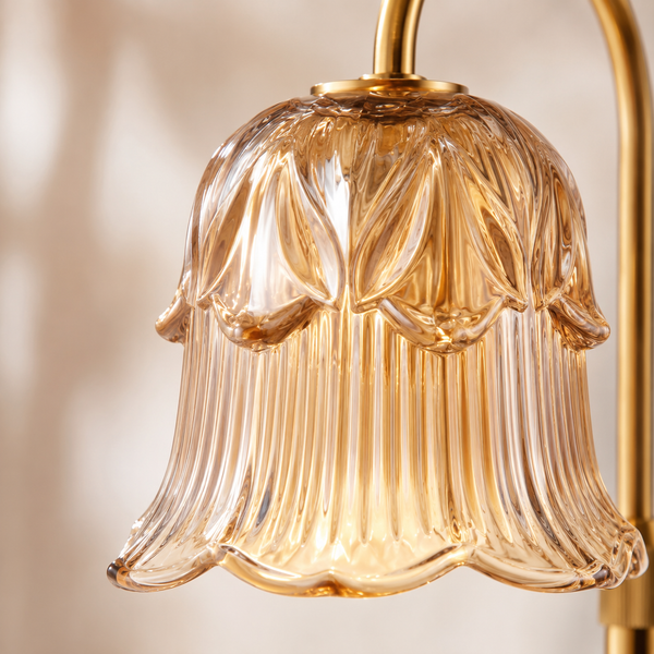 A close-up of a bell-shaped amber glass shade with vertical fluted detailing and a gold metal fixture arm at the top and right edge. Adjustable Height Candle Warmer Lamp — Brass Arch with Fluted Glass Shade