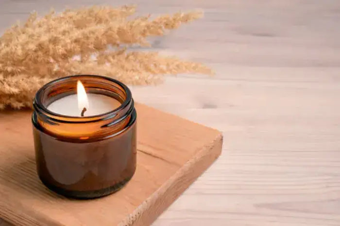 Lit candle in an amber glass jar on a wooden board with pampas grass