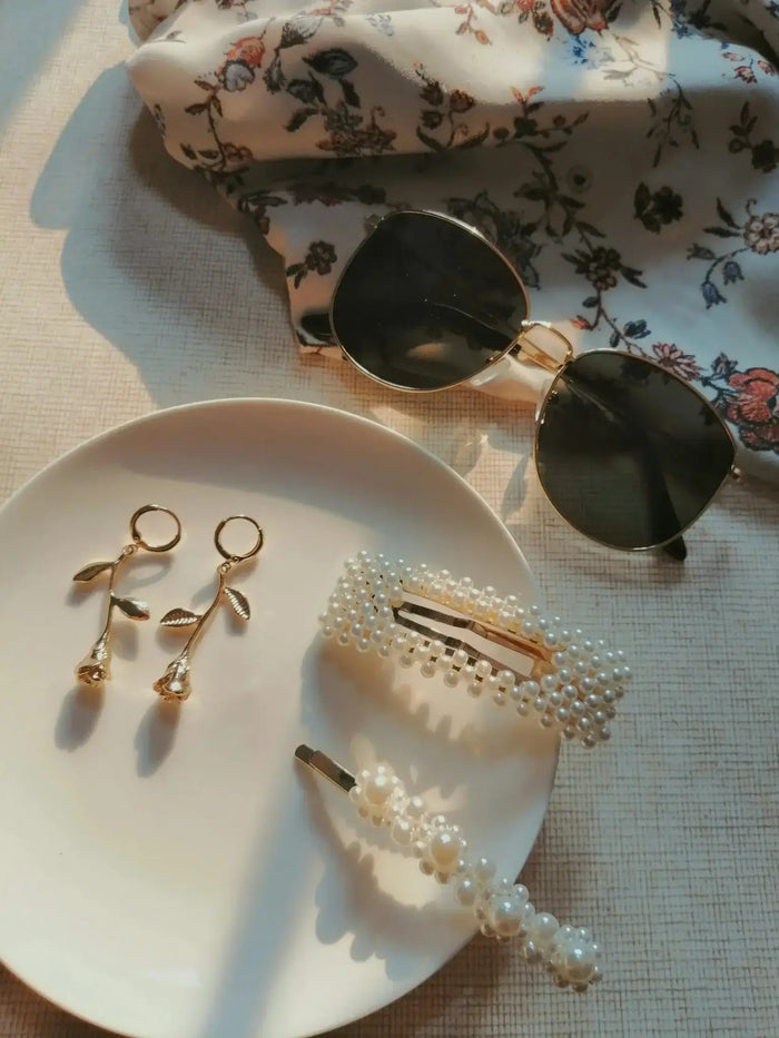 Plate with pearl hair clips and earrings next to sunglasses on a floral cloth