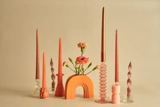 Colorful taper candles and an orange arch candle in glass holders with a small vase of carnations