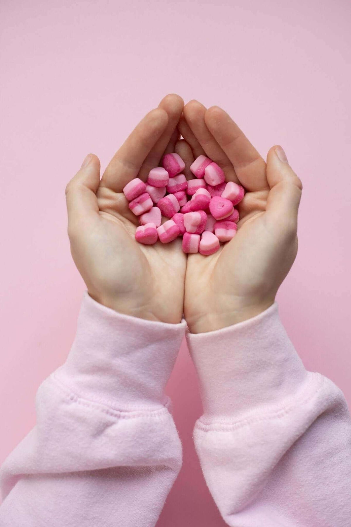 Two hands holding a small pile of pink wax pieces against a pink background