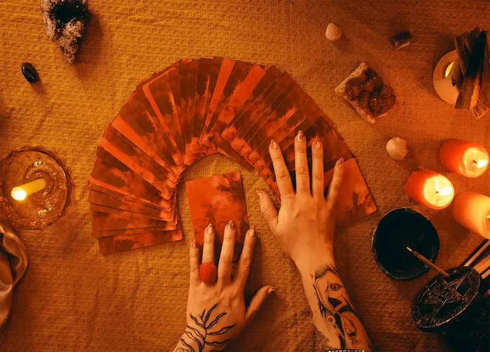 Hands arranging a fan of tarot cards beside lit candles and crystals
