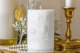 White candle with 'Joy' embossed, surrounded by gold and pearl decor