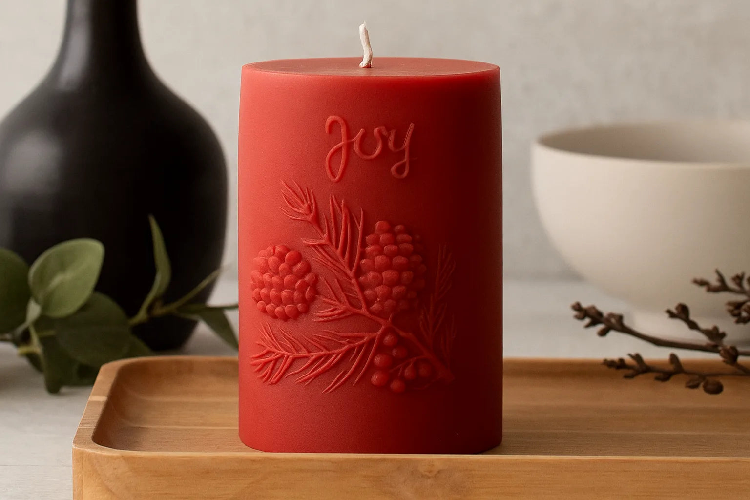 Red candle with 'Joy' and pine cone design on a wooden tray