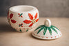 Decorative ceramic pot with red floral patterns on a neutral background