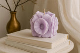 Purple floral candle on a stack of books with a gold vase in the background