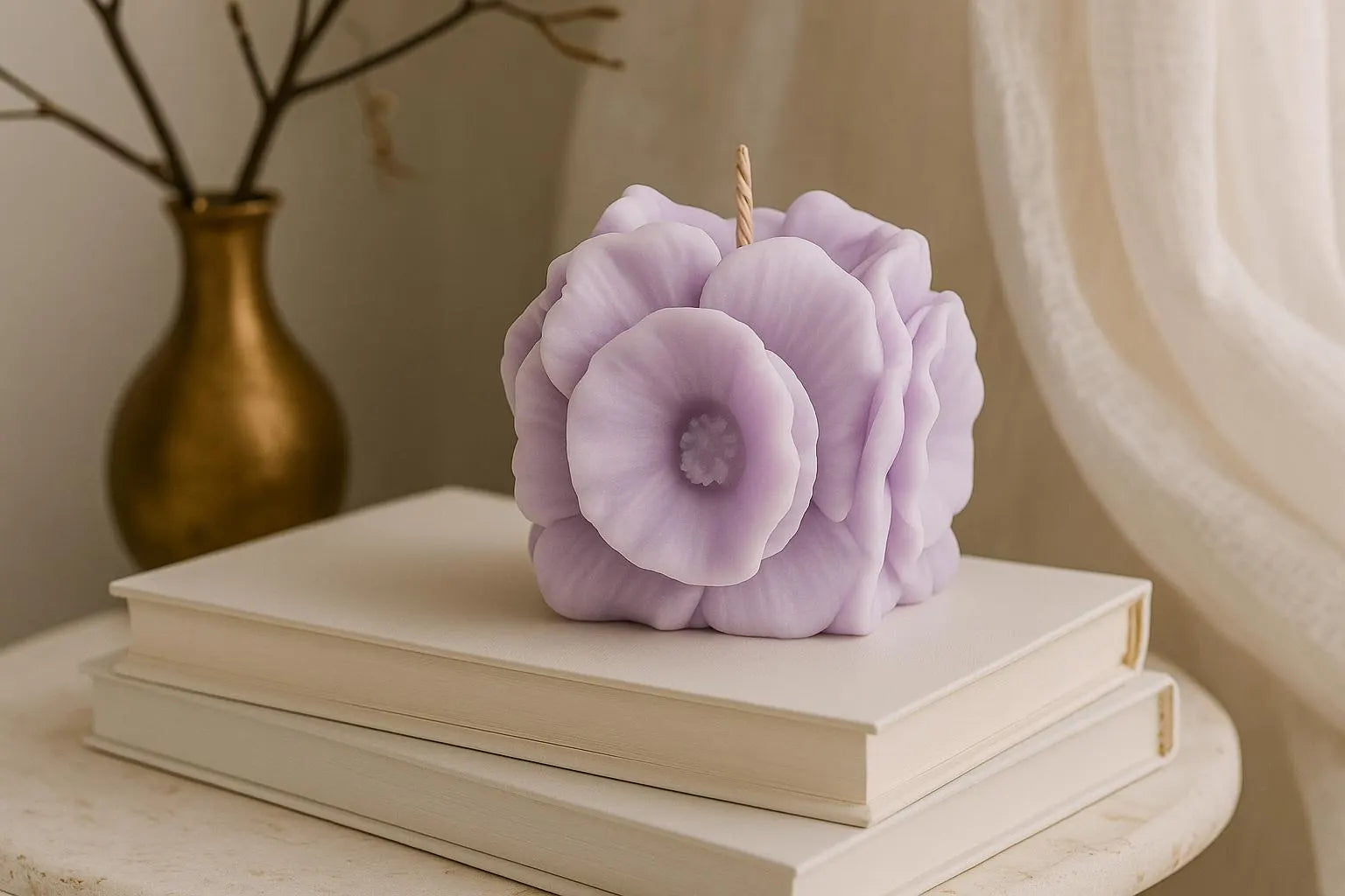 Purple floral candle on a stack of books with a gold vase in the background