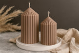 Two ribbed brown candles on a white plate with a neutral background