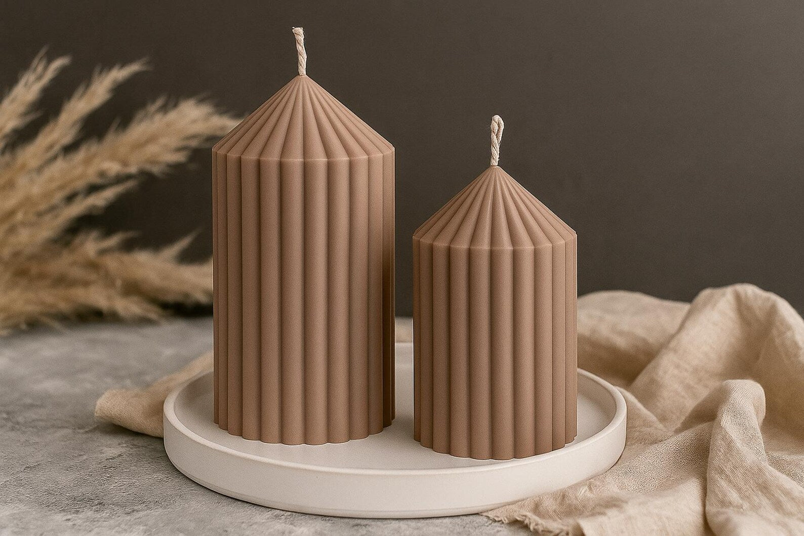 Two ribbed brown candles on a white plate with a neutral background