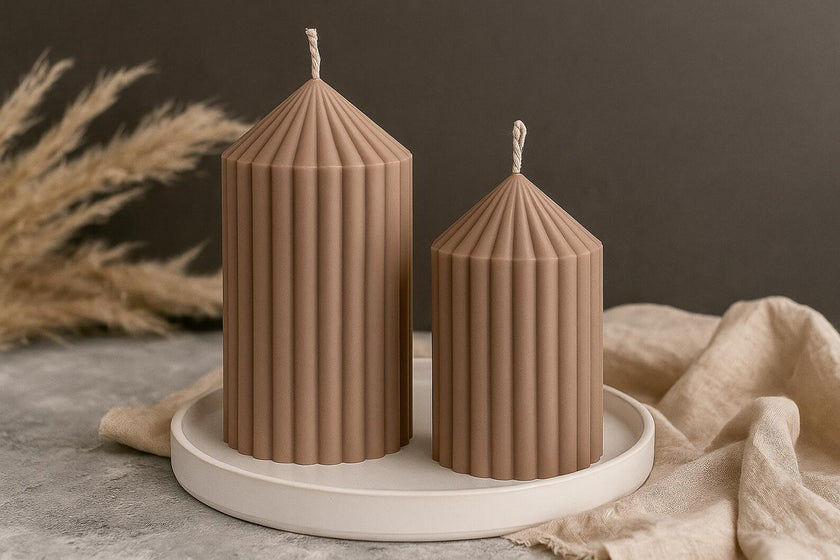 Two ribbed brown candles on a white plate with a neutral background