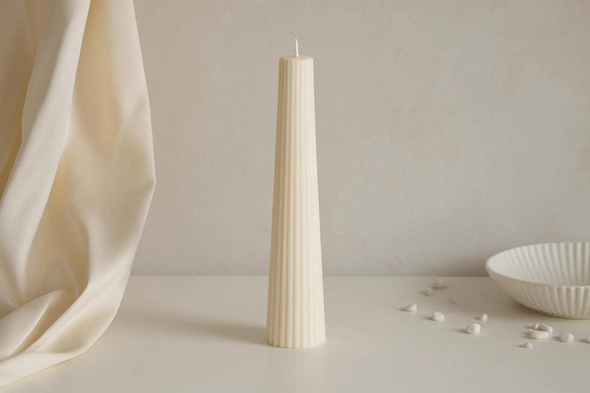 Tall, white, textured candle on a neutral background with a soft focus.