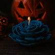 Black rose-shaped candle with a lit wick in front of a blurred jack-o'-lantern.
