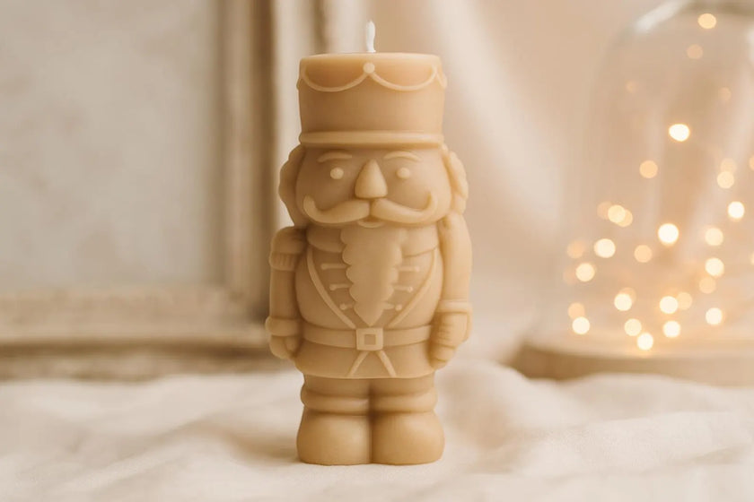 Candle shaped like a nutcracker figure on a soft surface with blurred lights in the background