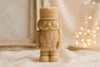 Candle shaped like a nutcracker figure on a soft surface with blurred lights in the background