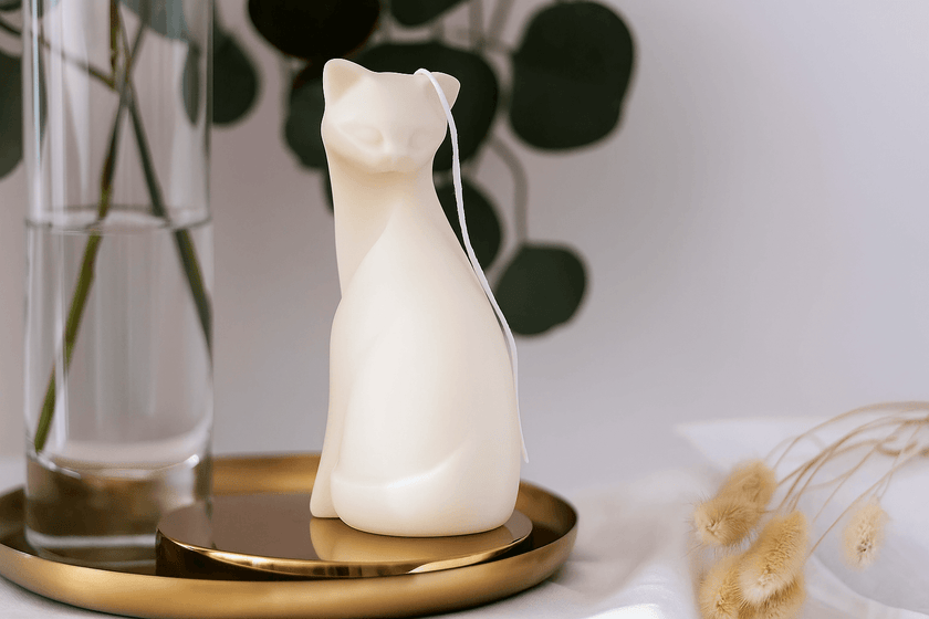 Cat-shaped white scented candle on a gold tray with a blurred background