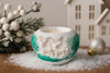Decorative candle holder with animal designs on a snowy surface with Christmas decorations.