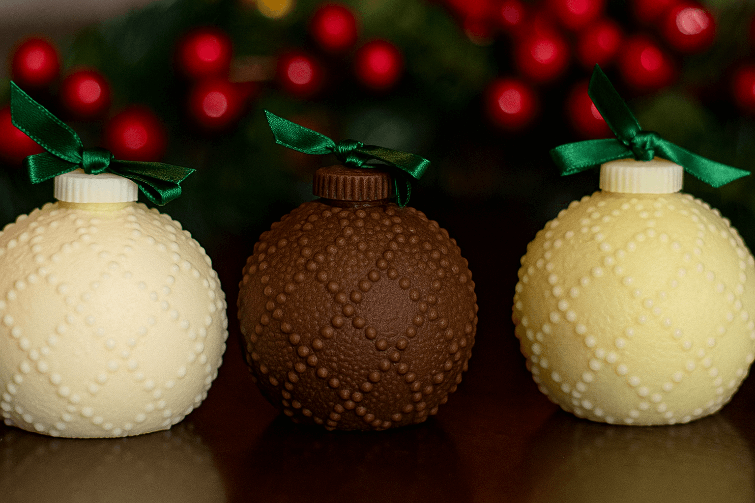 Three textured Christmas ornaments with green ribbons against a blurred festive background.