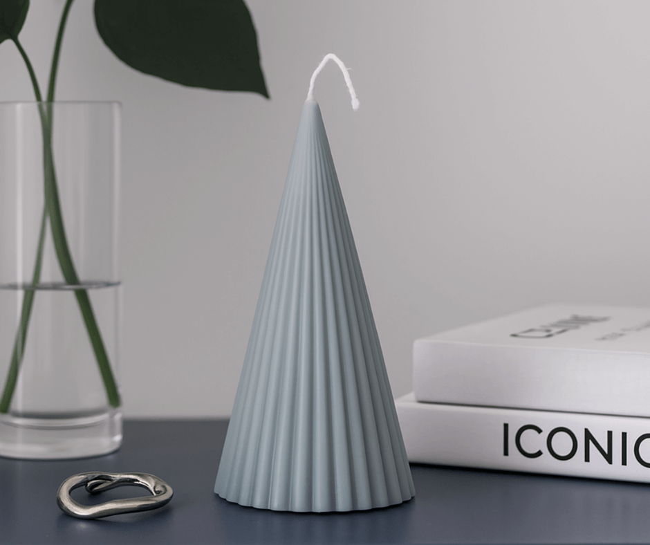 Cone-shaped handmade soy wax candles, one white and one dark gray, on a table with flowers.