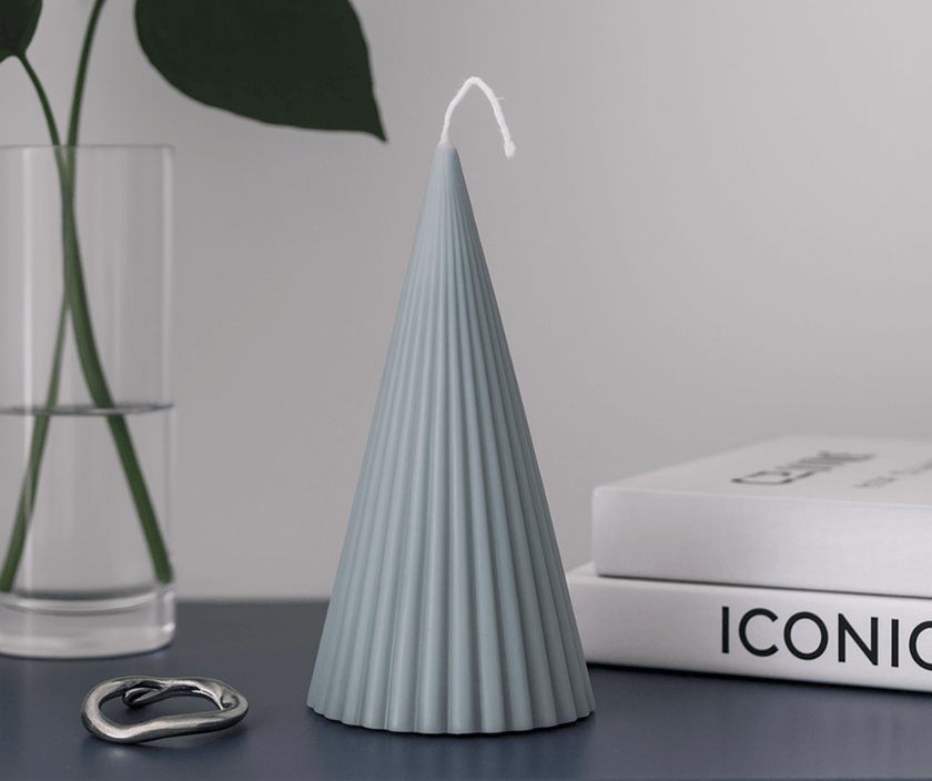 Cone-shaped handmade soy wax candles, one white and one dark gray, on a table with flowers.