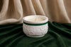 White ceramic incense burner with green rim on a green fabric background