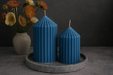Two blue striped candles on a gray tray with a vase of flowers in the background.