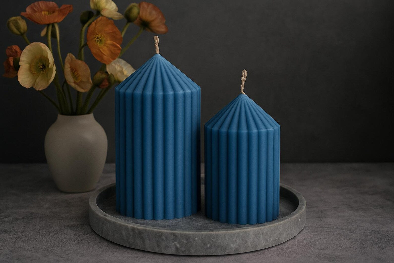 Two blue striped candles on a gray tray with a vase of flowers in the background.