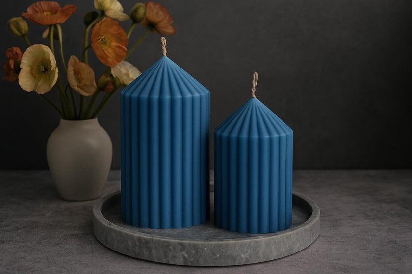 Two blue striped candles on a gray tray with a vase of flowers in the background.