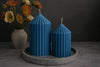 Two blue striped candles on a gray tray with a vase of flowers in the background.