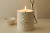 White candle with 'Cupid' Votive branding on a beige surface