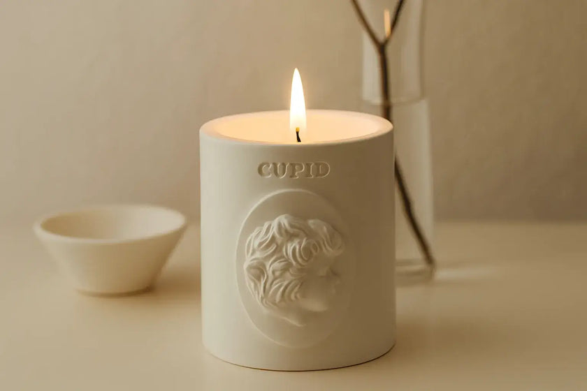 White candle with 'Cupid' Votive branding on a beige surface