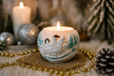 Decorative candle with a sleigh design on a table with Christmas decorations.