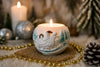 Decorative candle with a sleigh design on a table with Christmas decorations.