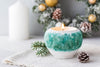 Teal and white ceramic candle holder with a lit candle on a light surface with decorative elements.