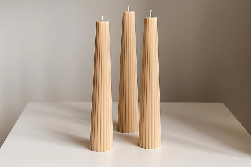 Three tall, thin, beige candles on a white surface with a neutral background