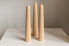 Three tall, thin, beige candles on a white surface with a neutral background