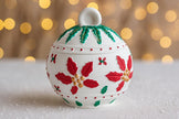 Decorative Christmas ornament with red holly leaves and green berries on a blurred light background