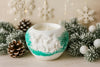 Decorative candle in a white holder with green accents, surrounded by Christmas decorations.