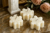 Four white snowflakes shaped candles on a marble surface with roses in the background.