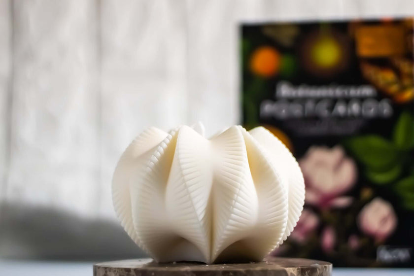 Geometrical scented candle on a wooden base with a book in the background, showcasing modern decorative style.