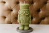 Green nutcracker-shaped candle on a gray base against a brown textured background