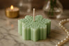Green snowflake-shaped candle with a lit wick on a marble surface, with a blurred background.