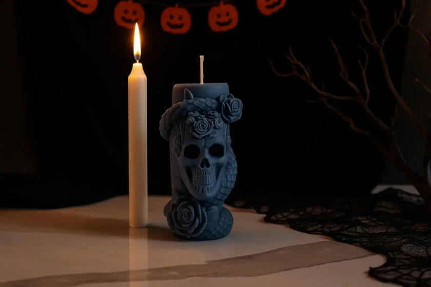 Black skull-shaped candle with a white candle against a dark background with Halloween decorations.
