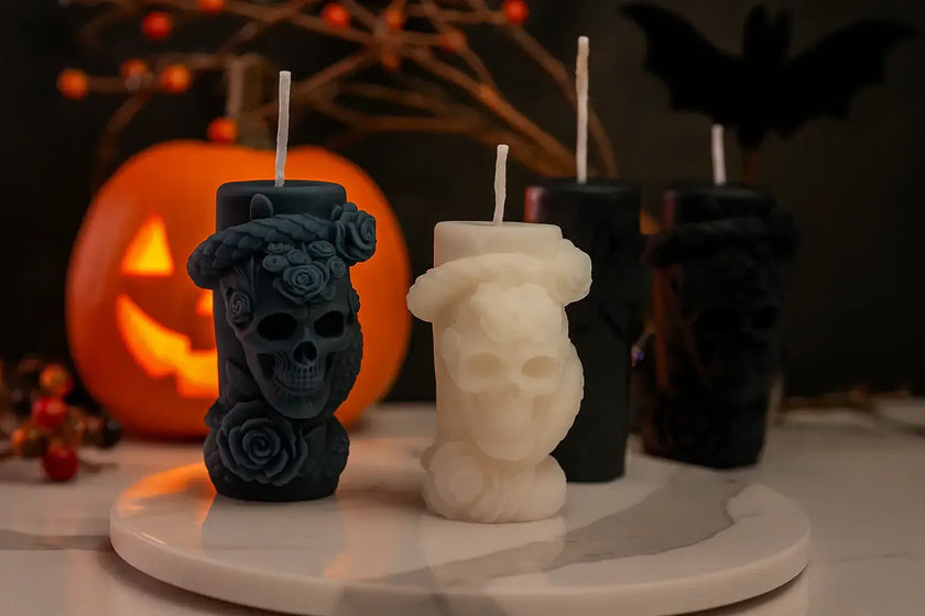Halloween-themed candles with skull and flower designs on a white surface with a dark background.